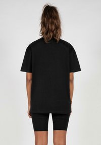 Black cotton t-shirt with short sleeves and a round neck, displayed from the back. Features a relaxed fit and plain design.