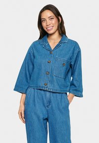 Denim jakna v svetlo modri barvi s skrajšanim dizajnom, gumbom spredaj, ovratnikom z izrezom in enim žepom na prsih. Ima dolge rokave in šivane detajle.