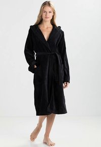 Črn kopalni plašč iz mehke tkanine, z nastavljivo kapuco, pasom in dvema sprednjima žepoma. Dolžina do kolen, sproščen kroj in teksturirana površina.