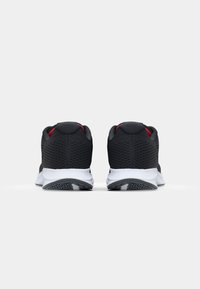 Baskets de sport noires avec une tige en maille, accent rouge près du talon, semelle intermédiaire blanche et semelle extérieure noire à motifs. Vue arrière affichée.