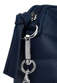 Tmavě modrá kožená kabelka zblízka s kovovým zipem a stříbrnými detaily, texturovaný povrch s viditelným šitím a detailem s třásněmi.