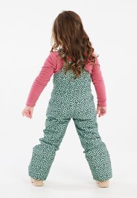 Salopette verde leggermente imbottita con pois neri, abbinata a un top a maniche lunghe rosa. Presenta spalline regolabili e vestibilità ampia.