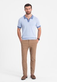 Polo light blue avec un col et des accents de manches contrastants, associé à un pantalon beige et des mocassins marron. Texture de tissu lisse.