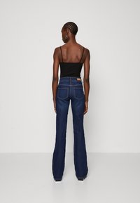 Hoch taillierte, ausgestellte dunkelblaue Jeans aus Denim mit fünf Taschen und einem Lederpatch auf der Rückseite. Getragen mit einem figurbetonten schwarzen Tanktop.
