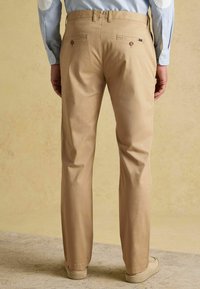 Beżowe chinosy o prostym kroju nogawek, z dwoma tylnymi kieszeniami zapinanymi na guziki, wykonane z gładkiej bawełnianej tkaniny.