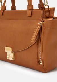 Sac à main en cuir marron avec double poignée, fermoir doré et détail de fermeture éclair latérale sur fond blanc.