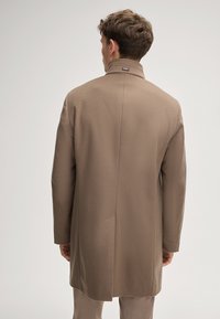 Bruine wolmix jas met hoge kraag en een enkele split aan de achterkant. Gladde textuur, getailleerde pasvorm en minimale details.