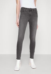 Jeans ajustados gris de denim, con un diseño entallado, bolsillos estándar y una cintura de altura media, combinados con botas blancas hasta el tobillo.