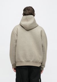 Sudadera con capucha beige de corte holgado, mangas oversize y dobladillo acanalado. Textura suave y cordón ajustable en la capucha.