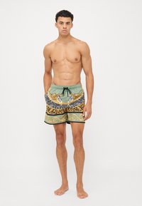 Badeshorts med grøn base og mønster af tiger- og leopardprint, elastisk talje og snøredetalje foran.