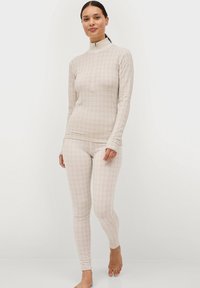Lichtbeige thermoset bestaande uit een langmouwtop met hoge kraag en bijpassende strakke leggings, beide met een reliëfpatroon.