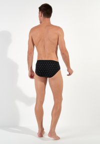 Zwarte zwembroekjes met witte cirkelpatronen, met een gladde, strakke pasvorm en een zachte elastische tailleband. Achteraanzicht weergegeven.