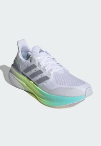 Biały but sportowy z oddychającą siateczkową cholewką, trzema szarymi paskami oraz gradientową podeszwą w odcieniach zieleni i niebieskiego. Posiada sznurowadła i grubą, miękko wyściełaną konstrukcję.