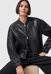 Giacca bomber in pelle nera con finitura texture, polsini a coste e chiusura frontale con zip. Design liscio e aderente con colletto arrotondato.