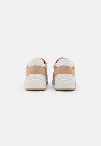 Sports shoes with beige suede upper and white leather accents. Textured rubber sole, rounded shape, padded heel for comfort.