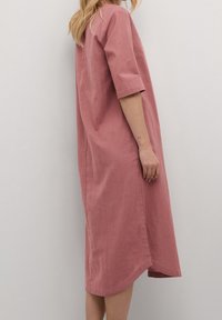 Rosa Leinenkleid mit kurzen Ärmeln, lockerer Passform, knielang, mit Seitenschlitzen und einem einfachen Rundhalsauschnitt. Glatte Textur.