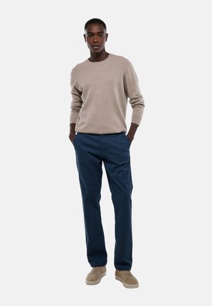 Pull en maille beige, pantalon bleu marine et baskets couleur tan. La tenue présente une coupe décontractée avec une texture douce, créant un look casual.