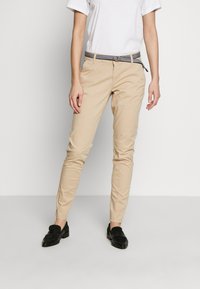 Chinos beiges coupe slim, avec une ceinture rayée. Confectionnés en coton, ils possèdent des poches latérales et une texture lisse. Associés à des mocassins noirs.