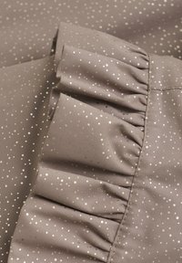 Bruine stof met een metallic gouden stippenpatroon. Heeft een gerimpelde rand en een soepele textuur, met een subtiele glans.