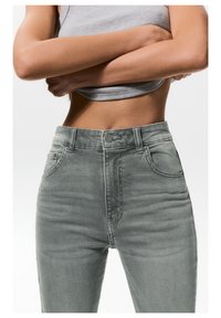 Jean en denim gris taille haute avec une silhouette ajustée, dotés de poches avant, d'une fermeture à bouton et d'une texture lisse.