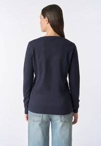Maglione navy a maglia con maniche lunghe, scollatura rotonda e orlo a coste. Indossato su jeans azzurri, la vista posteriore mostra una texture liscia e un design aderente.