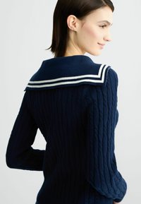 Maglione navy a trecce con un ampio colletto da marinaio con strisce bianche, che offre una superficie testurizzata e una silhouette attillata.