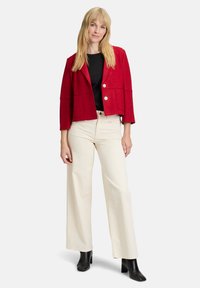 Blazer cropped in misto lana rossa con due tasche frontali, bottoni argentati e una maglietta nera. Abbinato a pantaloni crema a vita alta e stivaletti neri.