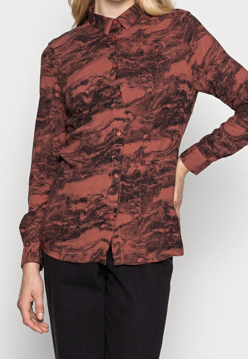 Camicia a maniche lunghe color ruggine con un motivo marmorizzato nero, chiusura frontale con bottoni e colletto. Realizzata in tessuto morbido con una texture liscia.