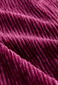Plüschiger, gerippter Stoff in tiefem Burgunderrot mit weicher Textur, der erhöhte, parallele Linien und eine glatte Oberfläche zeigt.