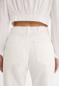 Bílé džíny z denimu se středním pasem, vybavené dvěma zadními kapsami a čistými švy. Štítek na pasu je viditelný.