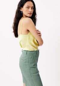 Geel satijnen top met dunne bandjes, gecombineerd met een groen-witte gestreepte pencil rok met zijzakken en een knoopdetail.