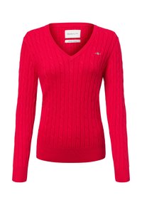 Roter Strickpullover mit V-Ausschnitt, versehen mit einem Zopfmuster. Lange Ärmel und gerippter Saum. Kleines Logo auf der linken Brustseite.