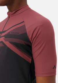 Maillot de cyclisme à manches courtes en bordeaux et noir, avec un col zippé, un motif géométrique et le logo Vaude sur la poitrine. Texture de tissu lisse.