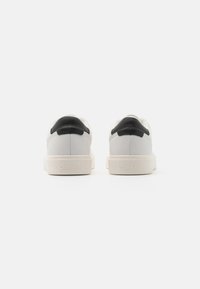 Sneakers bianchi in pelle con un accento nero sul tallone, presentano una superficie testurizzata e una suola spessa bianca. Logo "Calvin Klein" impresso sul lato.