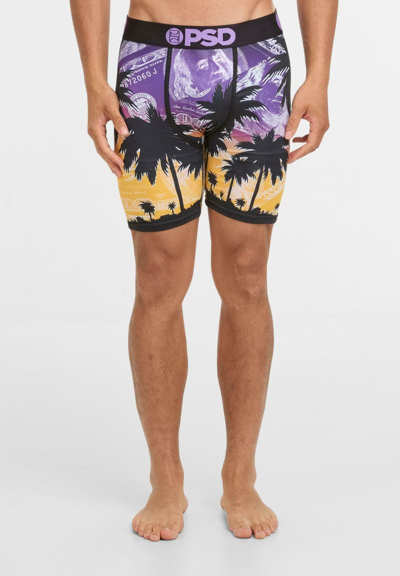 Hombre vistiendo bóxer coloridos con un atardecer púrpura y naranja, palmeras negras y una cinturilla con el logo de PSD.