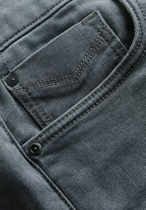 Szare dżinsy z przodu z kieszenią, widocznym przeszyciem i czarnym guzikiem, podkreślającym fakturę i jakość materiału.