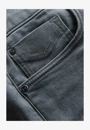 Szare dżinsy z przodu z kieszenią, widocznym przeszyciem i czarnym guzikiem, podkreślającym fakturę i jakość materiału.
