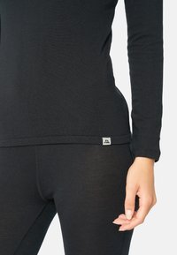 Zwarte longsleeve met een getailleerd ontwerp en een gladde textuur. Heeft een klein logo-label nabij de zoom. Gepaard met bijpassende zwarte legging.