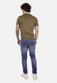 T-shirt in verde oliva a maglia con maniche corte e orlo ribattuto, abbinato a jeans di jeans blu chiaro e sneaker bianche, mostrato da dietro.