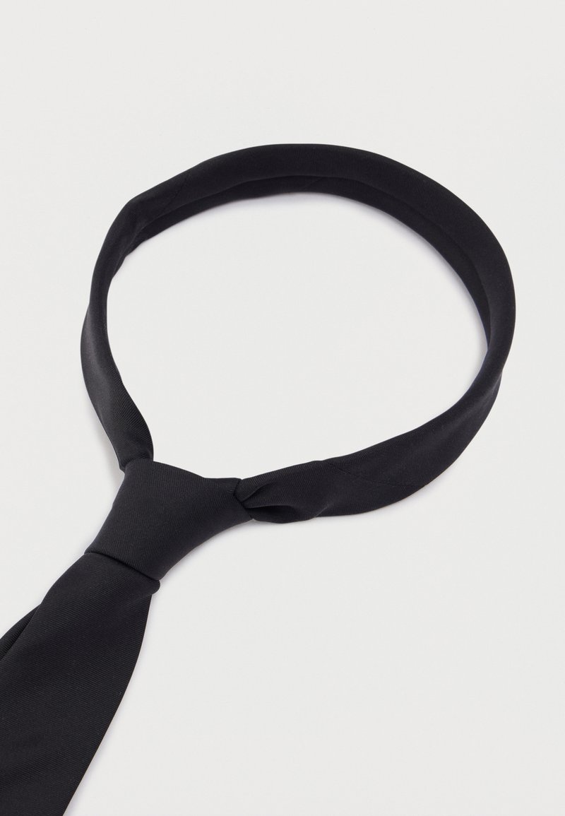 Cravate en tissu noir à texture lisse, présentant un design en boucle avec une extrémité nouée. La forme générale est allongée et effilée.