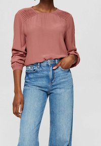 Rosa Bluse mit strukturierten Falten an den Schultern, langen Ärmeln mit elastischen Bündchen, kombiniert mit hellblauen High-Waist-Jeans.