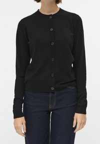 Black cardigan made of soft fabric, featuring a round neck, long sleeves, and six-button closure. Paired with dark denim pants.