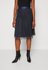 Jupe plissée navy avec des fils métalliques, ourlet transparent et une taille lisse. Associée à des bottines noires à bout pointu.