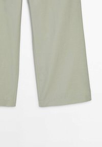 Pantalon large vert clair montré de la mi-cuisse à l’ourlet sur fond blanc.