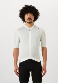 Maillot de cyclisme à manches courtes en gris clair avec une fermeture éclair à l'avant, en tissu texturé et à la coupe ajustée, associé à un short de cyclisme noir.