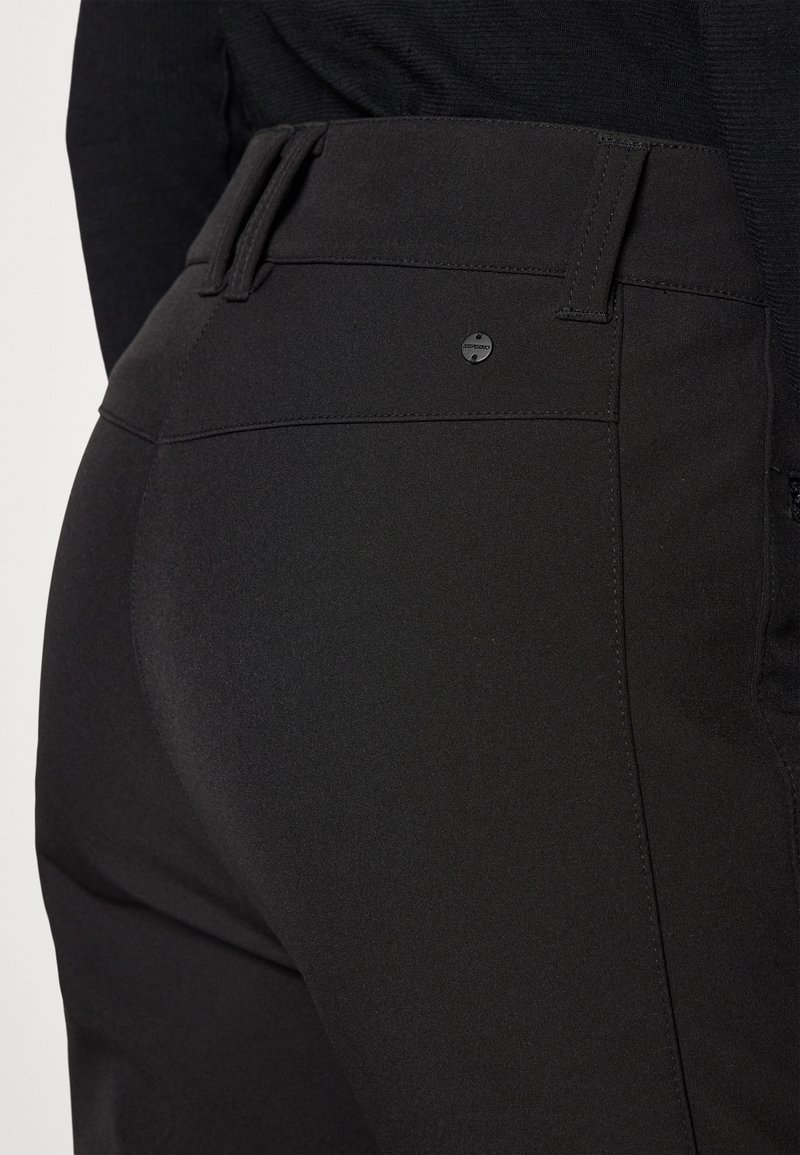 Schwarze Stretchhosen verfügen über einen figurbetonten Schnitt, eine glatte Textur, gesteppte Nähte und ein kleines, kreisförmiges Logo-Element am hinteren Bündchen.