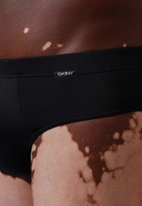 Schwarze Badehose mit glatter Textur, ausgestattet mit einem elastischen Bund in Markenqualität. Die Haut zeigt unterschiedliche Farbtöne mit ausgeprägten Mustern.