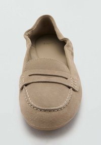 Zapato slip-on de ante beige con punta redondeada, acentos decorativos de costura y textura suave. Diseño simple y sin adornos.