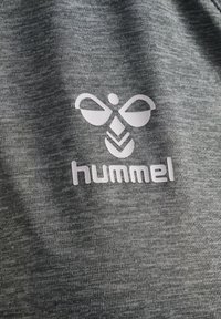 Grå, strukturert tyg med en fremtredende, hvit Hummel-logo som har et stilisert bikledesign og sentrert tekst.