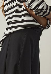 Maglia a maniche lunghe a righe bianche e nere con orlo arrotondato abbinata a pantaloni neri su misura, che mostrano trame lisce e linee pulite.